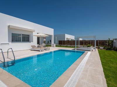 Bungalow blanco moderno con piscina clara, tumbonas y césped bajo cielo azul.