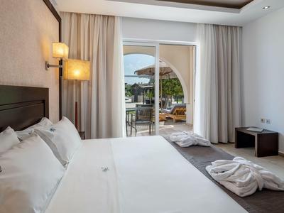 Modernes Hotelzimmer mit großem Bett, Balkon und Blick auf einen Poolbereich.