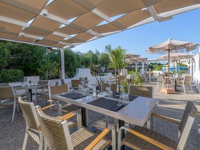 Área exterior cubierta de un hotel con mesas, sillas y sombrillas bajo cielo despejado.