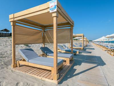 Strandliegen mit Sonnendach auf einem Sandstrand unter blauem Himmel.