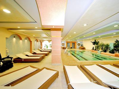 Área interior de un hotel de bienestar con piscina y tumbonas, iluminación clara y ambiente relajado.