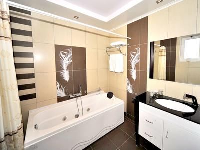 Baño moderno con bañera blanca, espejo, lavabo y azulejos marrones.