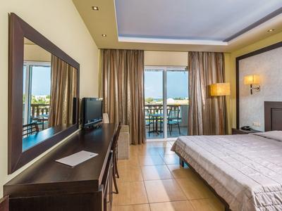 Habitación de hotel con cama doble, escritorio, silla, espejo grande y balcón con vista al mar.