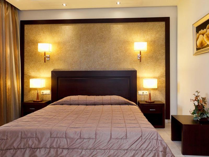 Habitación de hotel luminosa y acogedora con cama doble, mesitas de noche, lámparas de pared y arte decorativo.