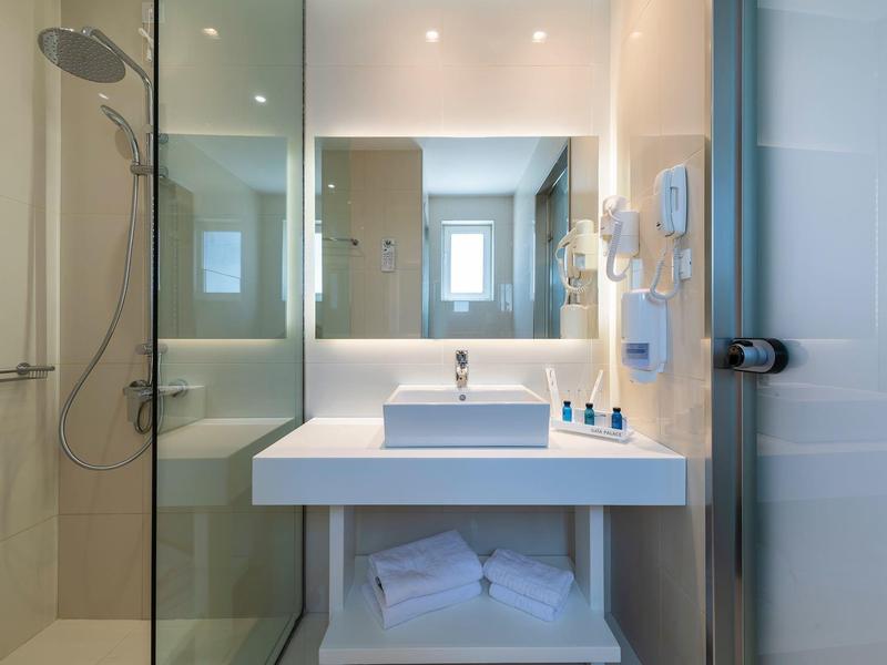 Baño moderno con lavabo blanco, ducha de vidrio y paredes claras.