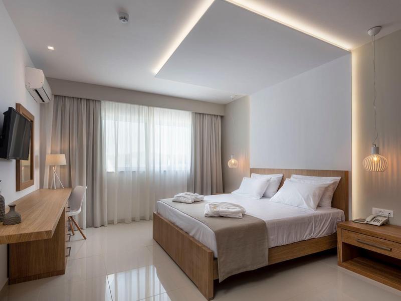 Habitación de hotel moderna con cama doble, televisión y grandes ventanas con cortinas.