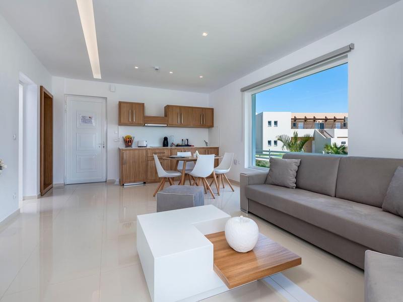 Sala de estar moderna con sofá, mesa de centro y área de comedor adyacente con muebles de madera.