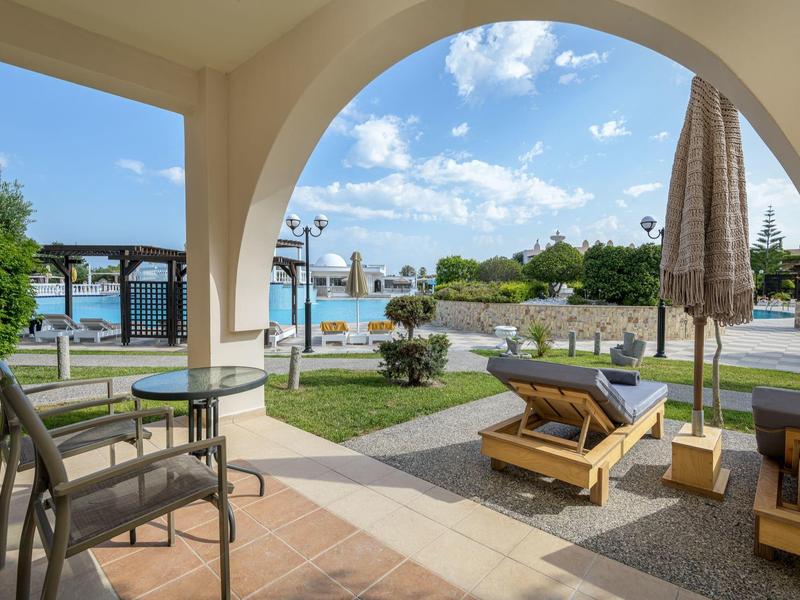 Terraza con muebles de jardín y vista a la piscina y al mar en un resort vacacional.