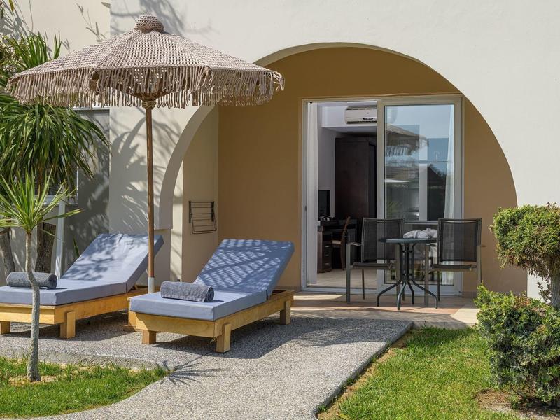 Dos tumbonas con cojines azules bajo una sombrilla frente a una habitación de hotel con arco redondo.