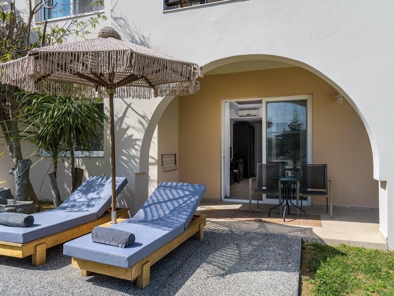 Terraza de hotel con dos tumbonas y sombrilla frente a una ventana arqueada, suelo de piedra arenisca y césped verde.