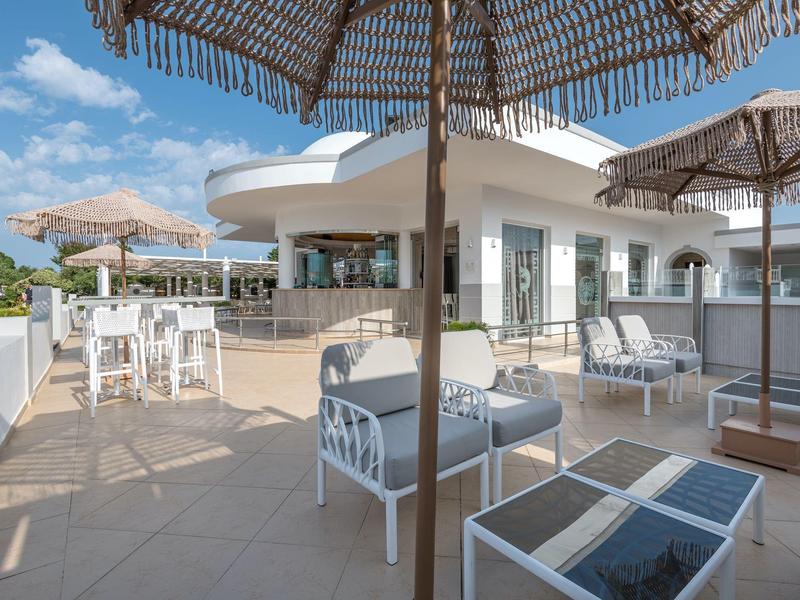 Área moderna de terraza de hotel con asientos y tumbonas bajo sombrillas durante el día.