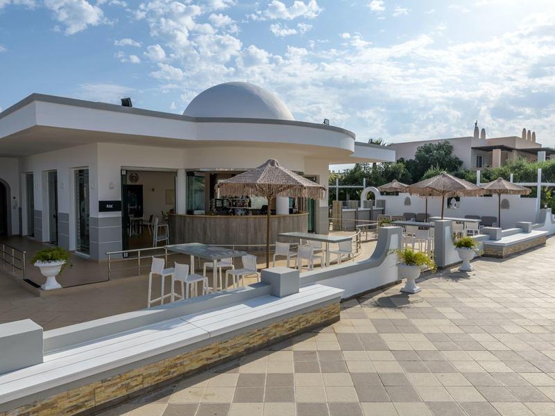 Área exterior moderna de un hotel con asientos y sombrillas bajo un cielo azul.