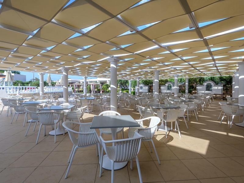 Amplia terraza con mesas y sillas blancas bajo una sombrilla sombreada.