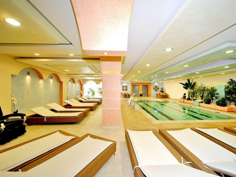 Área interior de un hotel de bienestar con piscina y tumbonas, iluminación clara y ambiente relajado.