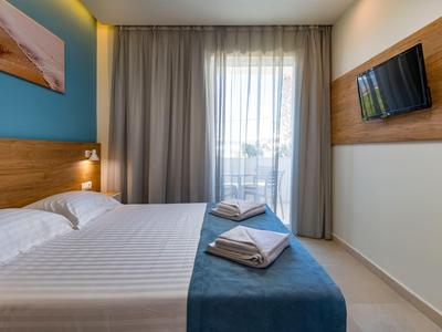 Kleines Schlafzimmer mit Doppelbett, blauer Wand, Holzdekor und kleinem Balkon mit Vorhängen.