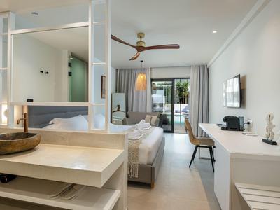 Helles, modernes Hotelzimmer mit Doppelbett, Schreibtisch, Deckenventilator und Balkon mit Meerblick.