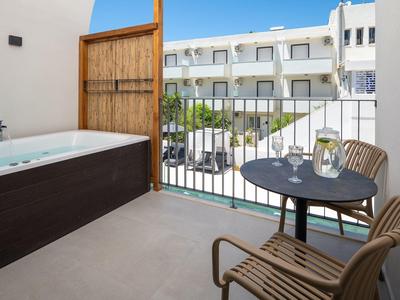 Balkon mit dunkler Badewanne, zweisitzigem Tisch und zwei Holzstühlen vor weißem Mehrfamilienhaus.
