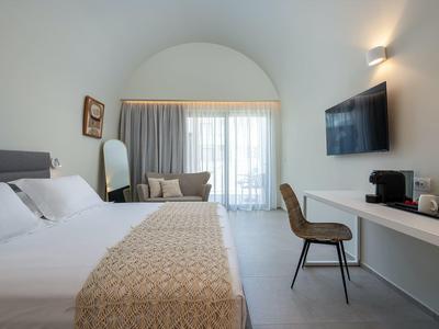 Modernes Schlafzimmer mit großem Bett, Schreibtisch, Stuhl, Fernseher und bodentiefem Fenster mit Vorhang.