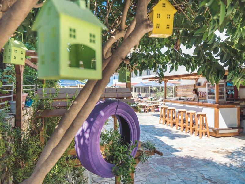 Barevné budky pro ptáky a fialová pneumatika visí na stromě vedle venkovního baru.