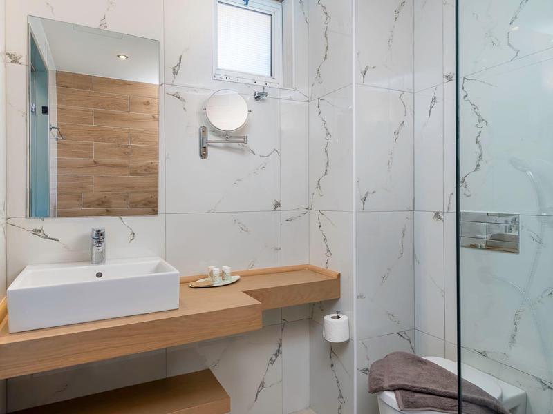 Moderní koupelna s bílým umyvadlem, dřevěnou policí a skleněnou sprchou.