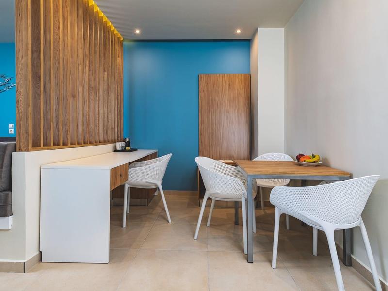 Moderní jídelní kout s bílými židlemi, dřevěnými stoly a modrou zdí v hotelovém pokoji.