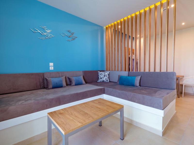 Moderní obývací pokoj s modrou zdí, velkou šedou rohovou pohovkou a dřevěným stolem.