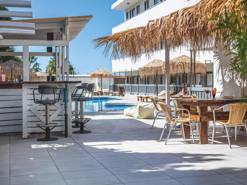 Terasa s stoly, židlemi a slunečníky vedle hotelového bazénu za slunečného dne.