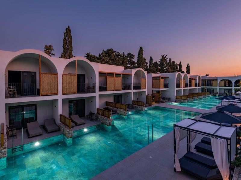 Moderní hotelový komplex s bazénem a odpočinkovými zónami za soumraku.