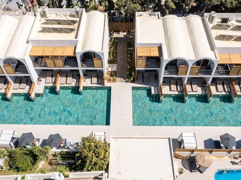 Letecký snímek hotelu se dvěma bazény a slunečníky mezi bílými budovami.