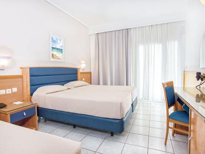 Helles Hotelzimmer mit zwei Betten, hellblauen Stühlen und einem Schreibtisch aus Holz.
