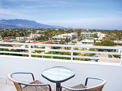 Balkon mit Tisch und zwei Stühlen, Blick auf Stadt, Berge und Meer bei klarem Himmel.