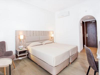 Helles Schlafzimmer mit großem Bett, Nachttischen, Schreibtisch und Fernseher an weißer Wand.