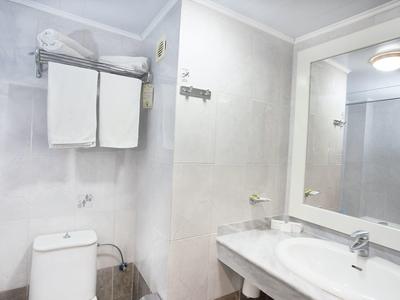 Weiß gefliestes Badezimmer mit Toilette, zwei Hängehandtüchern und Waschbecken mit Spiegel.