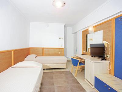 Einfaches Hotelzimmer mit zwei Betten, Holzverkleidung, Fernseher und blau-gelben Möbeln.