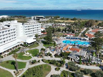 Großes Resort mit weißen Gebäuden, Pool, grünen Gärten und Blick auf das blaue Meer.