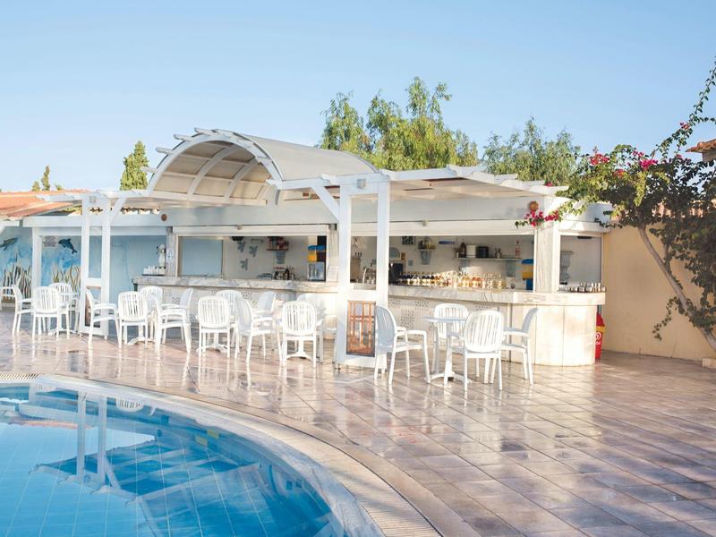 Venkovní bar s bílými židlemi vedle bazénu pod jasnou oblohou.