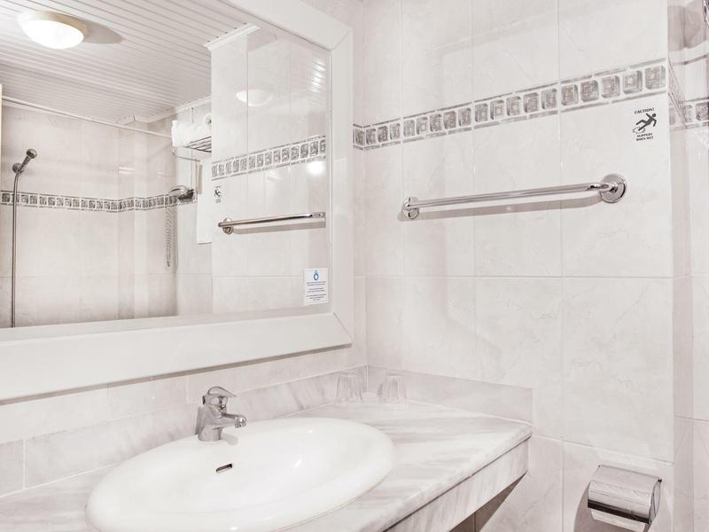 Světla koupelna se umyvadlem, velkým zrcadlem a držákem na ručníky na stěně.