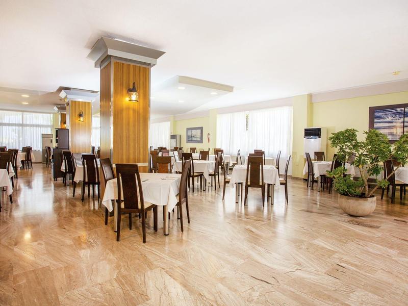 Světlá a prostorná jídelna se světlým dřevěným nábytkem a velkými okny.