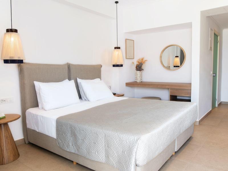 Moderně zařízený hotelový pokoj s velkou manželskou postelí, nočním stolkem a jednoduchou výzdobou.