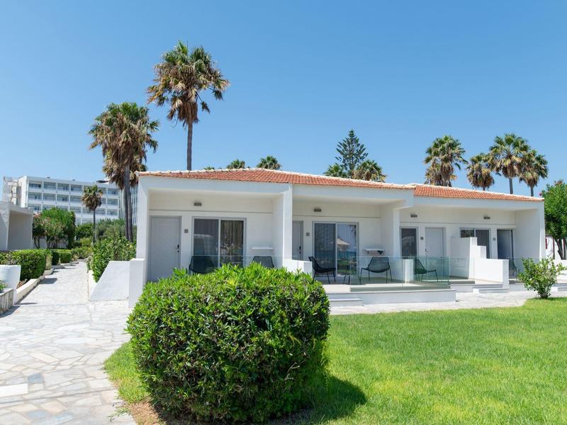 Bílý rekreační dům s terasou obklopený zeleným trávníkem a palmami.