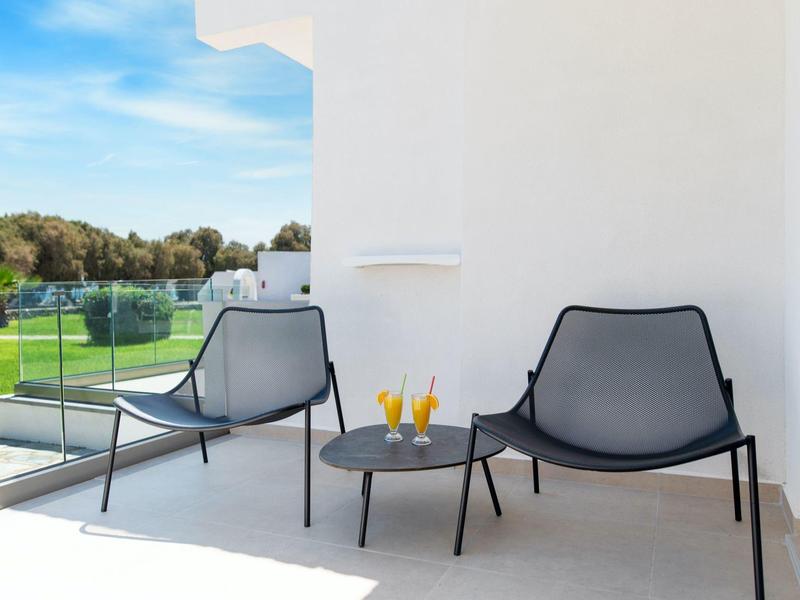 Dva moderní křesla a malý stůl s nápoji na slunné terase s výhledem na zeleň.