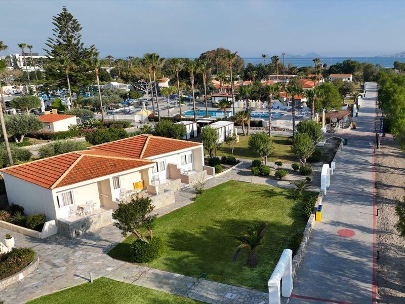 Pohled na přímořskou promenádu s vilami, palmami a mořem pod jasnou oblohou.