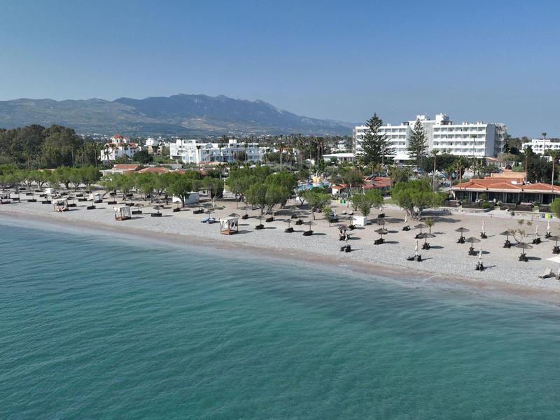 Pláž s lehátky a budovami podél pobřeží před horami pod jasnou oblohou.