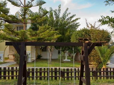 Houten schommel met twee zitplaatsen in tuin met bomen en hek op de achtergrond.