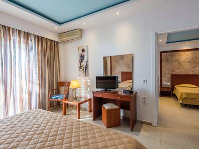 Moderne hotelkamer met tweepersoonsbed, tv, bureau en uitzicht op aangrenzende slaapkamer.