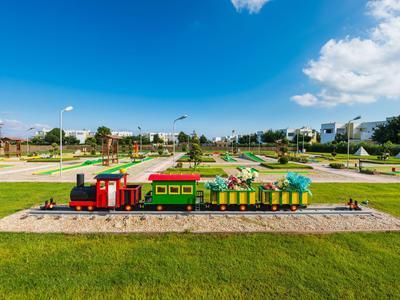 Bunter Freizeit-Zug fährt auf Schienen durch einen Park mit grüner Wiese und blauem Himmel.