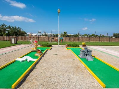 Minigolfanlage mit zwei Bahnen, umgeben von Sand und Zäunen bei klarem Himmel