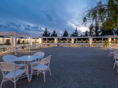 Abendliche Terrasse eines Hotels mit weißen Stühlen und Tischen unter beleuchteten Pergolen.