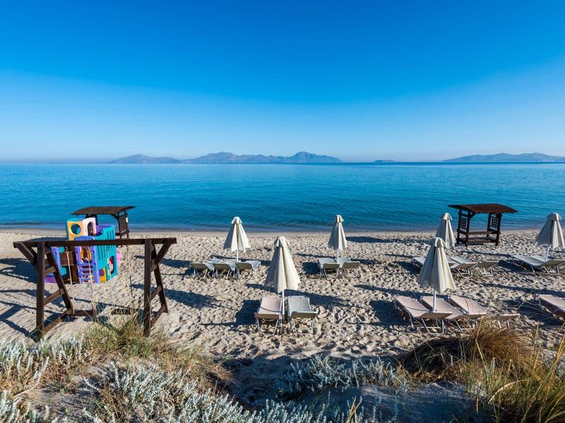 Leeg zandstrand met parasols en reddingtoren bij kalme zee onder heldere lucht.