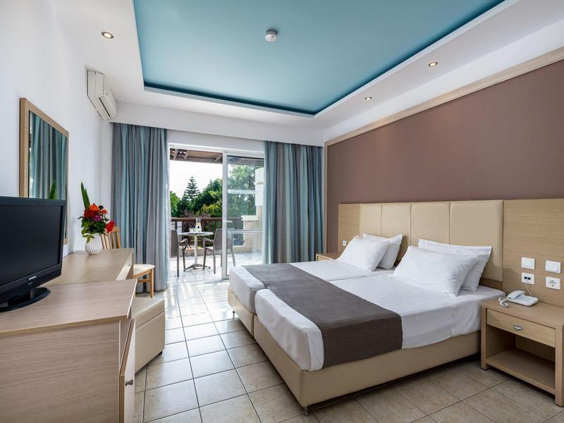 Modern hotelkamer met groot bed, tv en balkon met uitzicht op groen.